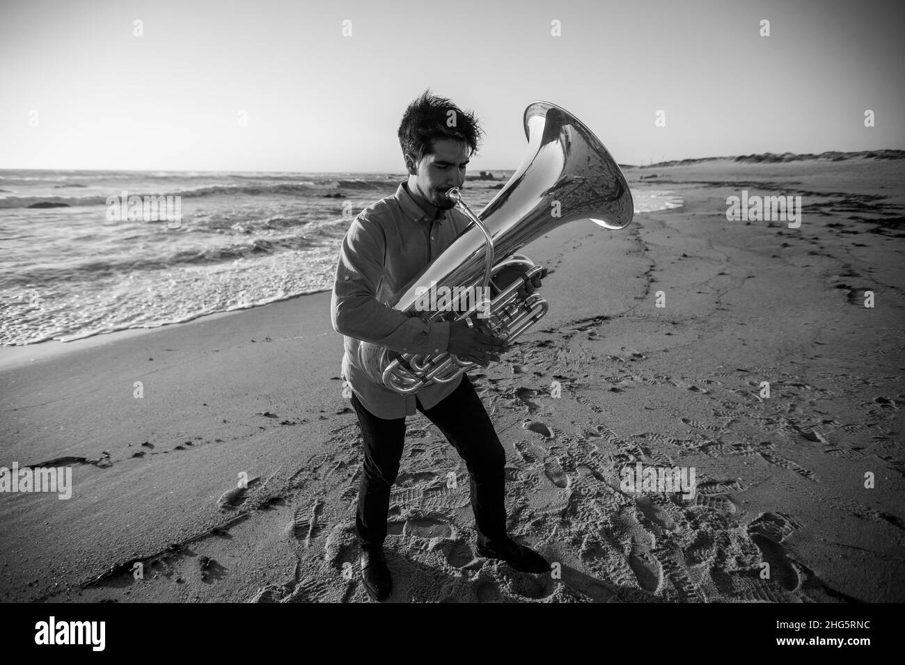 Musiker mit einer Tuba, die in der Nähe des Ozeans steht. Schwarzweiß-Foto. Stockfoto