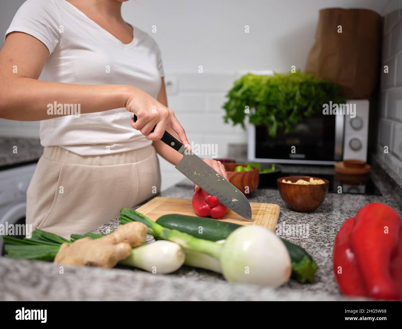 Seitenansicht einer Frau, die mit einem Küchenmesser einen roten Pfeffer spaltet Stockfoto