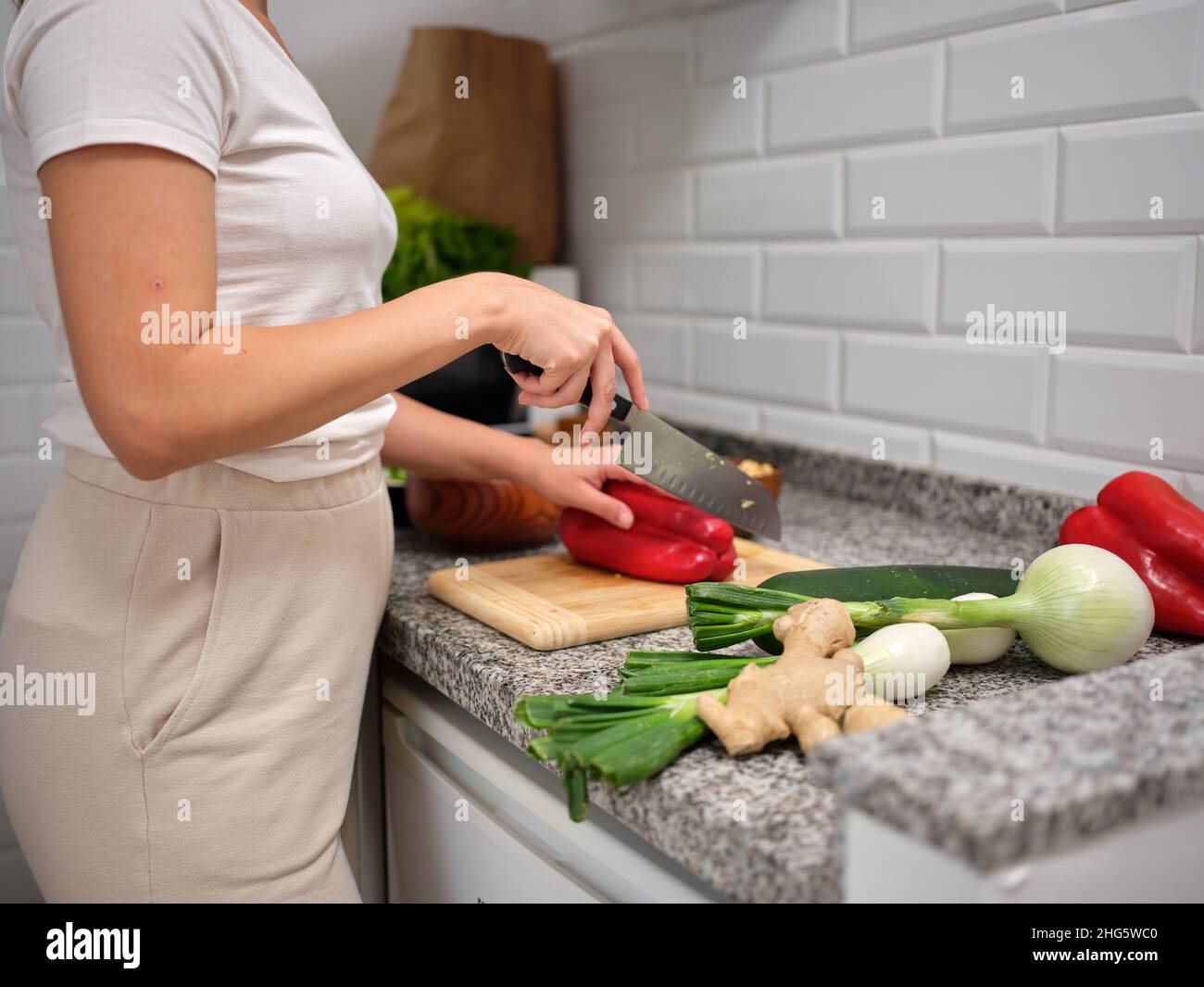 Erwachsene Frau, die ein Gemüsegericht ausarbeitet und einen roten Pfeffer auf einem Holzbrett spaltet Stockfoto