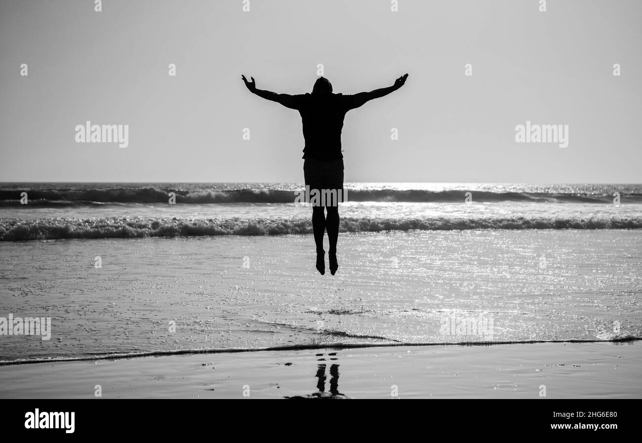 Silhouette des athletischen Mannes springen mit erhobenen Händen am Sommerstrand, Inspiration Stockfoto