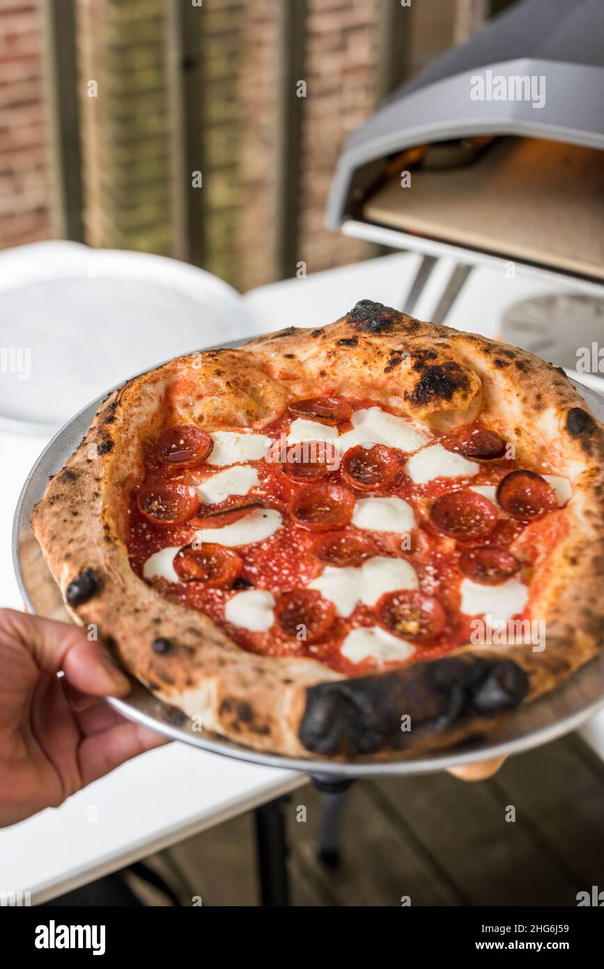 Pizzaiolo mit frischem Pfefferoni-Kuchen, der im Pizzaofen im Freien zubereitet wird Stockfoto