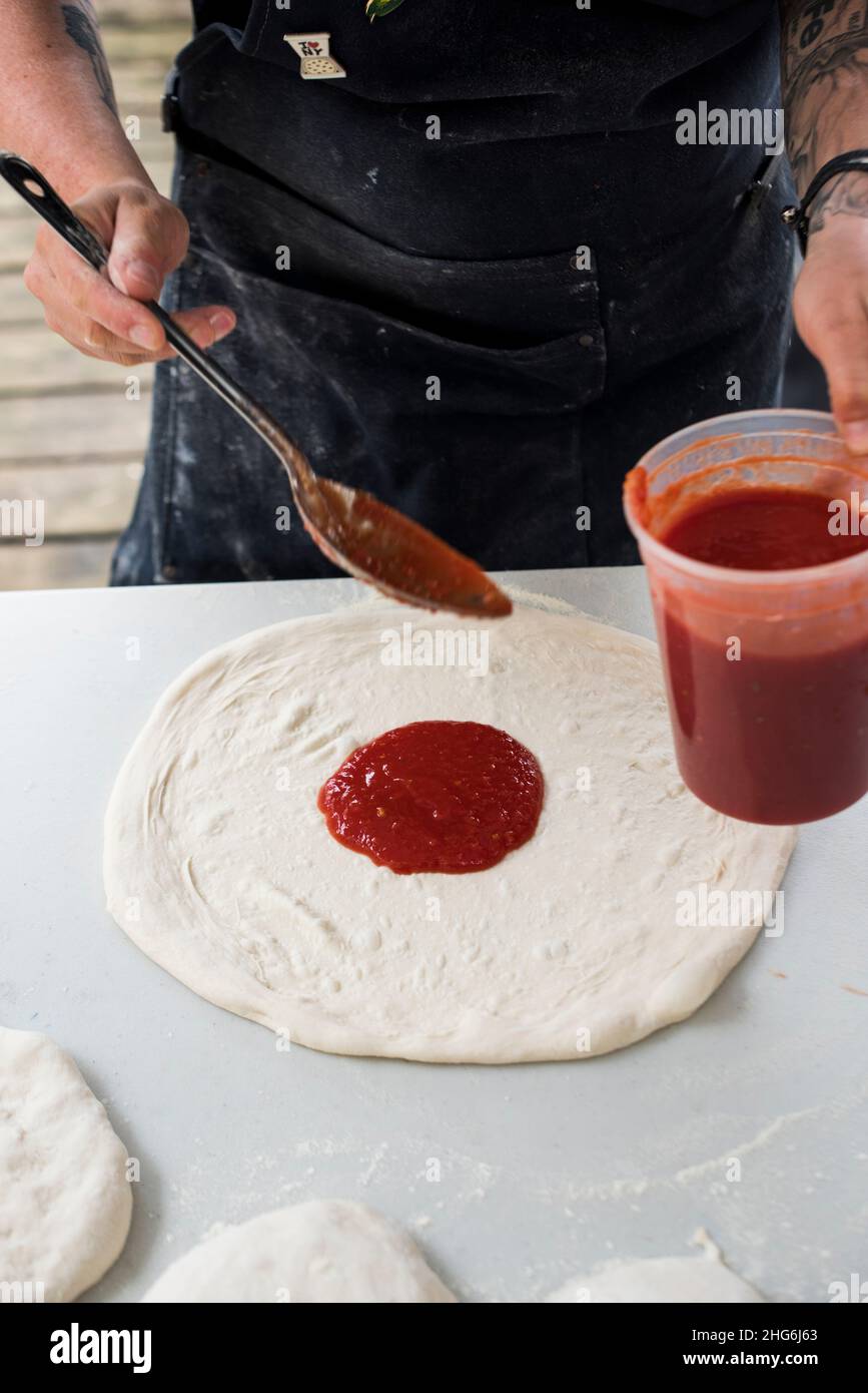 Pizzahersteller verteilt Sauce auf Pizzabasis Stockfoto