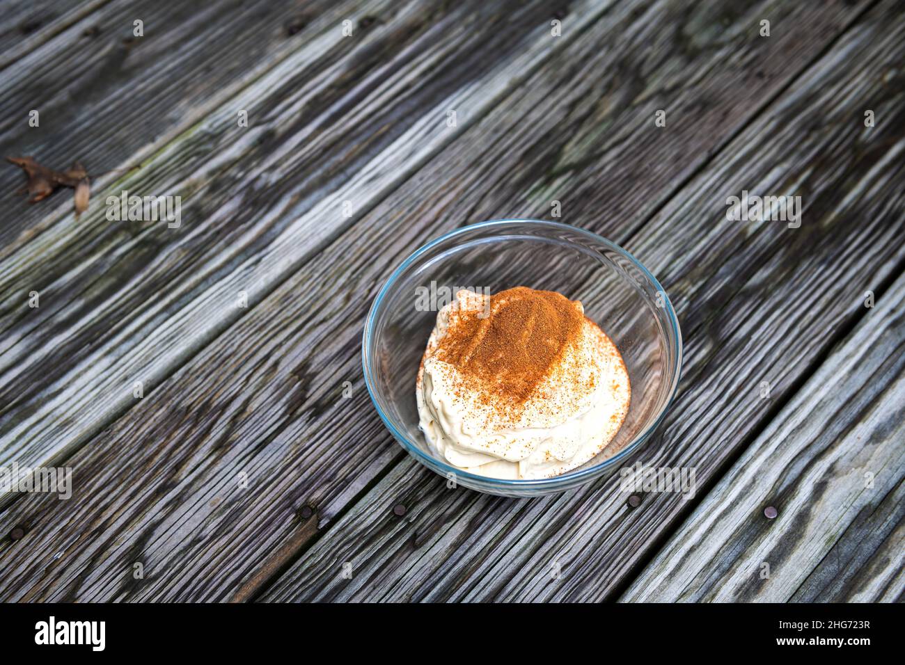 Bananeneis draußen auf der Terrasse oder rustikaler Holztisch im Hintergrund mit Glasschüssel aus hausgemachtem rohem veganem, schönem Creme mit Zimt Stockfoto