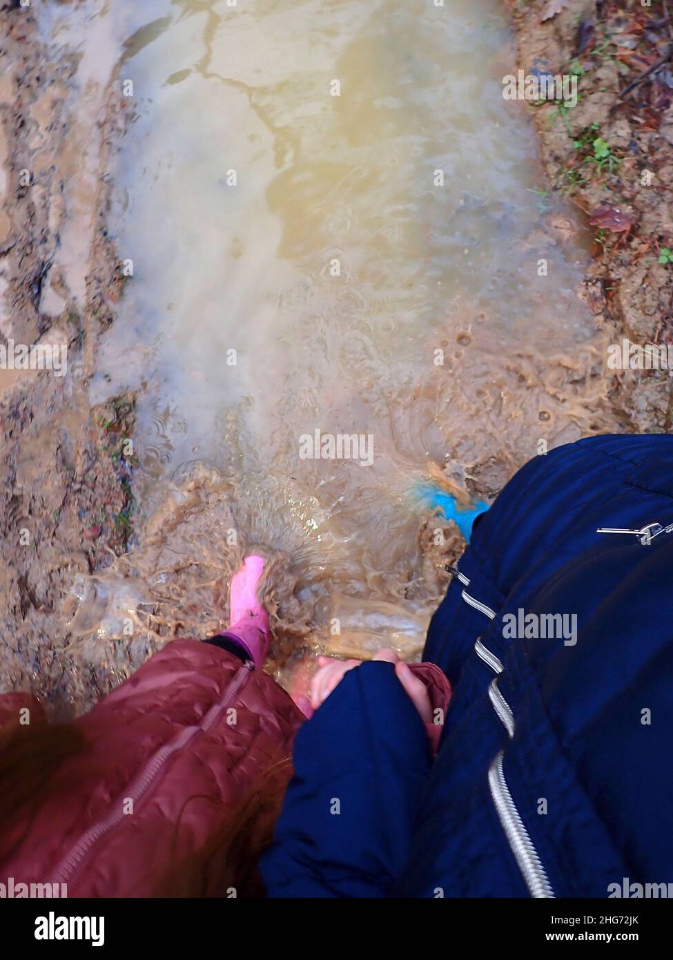 Frühlingslache.Pfütze gehen. Füttel in blauen und rosa Gummistiefeln im Frühjahr schlammiges Wasser.Schritte im Wasser. Gummistiefel geht durch die Pfützen. Schlamm Stockfoto