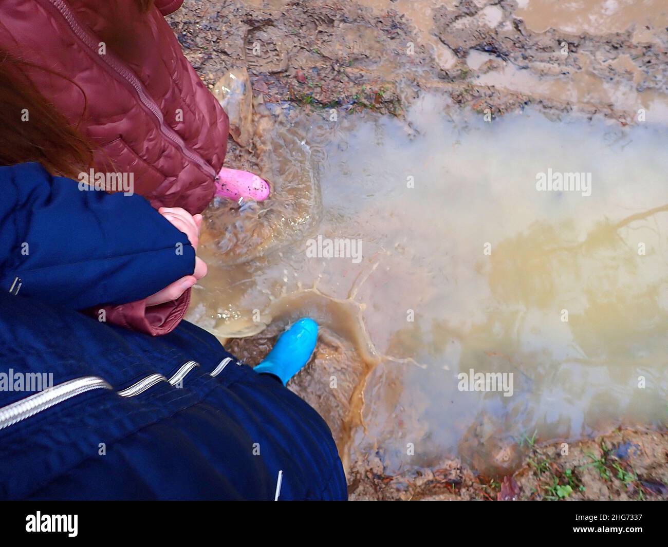 Frühlingslache.Pfütze gehen. Füttel in blauen und rosa Gummistiefeln im Frühjahr schlammiges Wasser.Schritte im Wasser. Gummistiefel geht durch die Pfützen. Schlamm Stockfoto