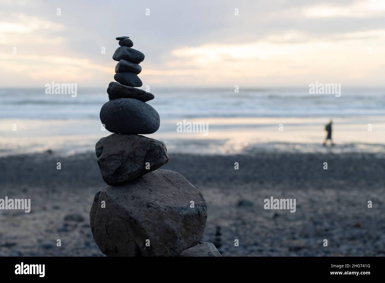 Zen stapelt Steine während des Sonnenuntergangs am Strand, der mit Steinen bedeckt ist, die bei Ebbe nach dem Vulkanausbruch von Tonga an Land gespült wurden. Stockfoto