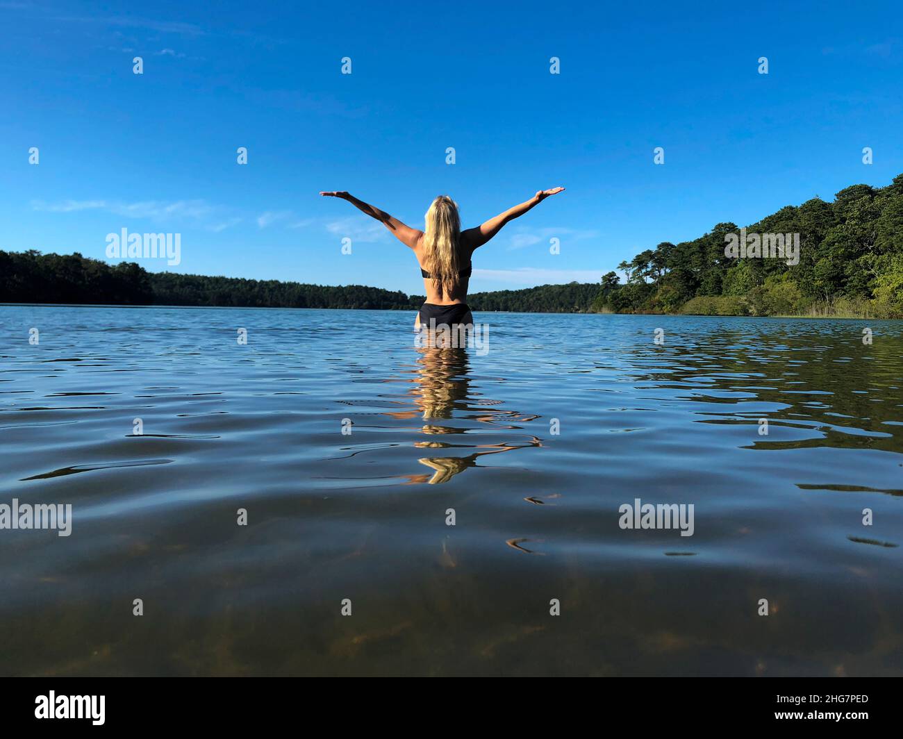 Blonde Frau von hinten im Teich mit ausgestreckten Armen Stockfoto
