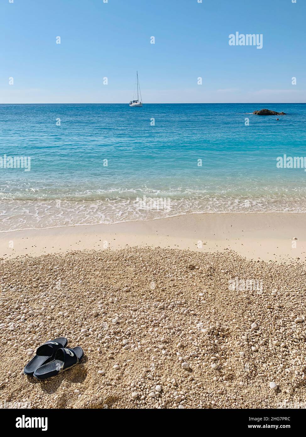 Nike Pantoffeln am Strand mit Segelboot auf dem Meer, Porto Katsiki, Stockfoto