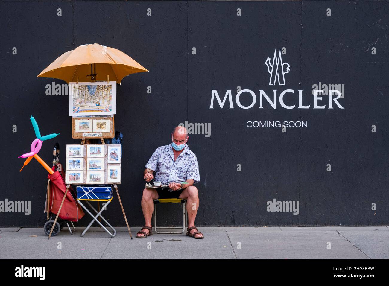 Ein Maler, der eine Gesichtsmaske trägt, arbeitet auf dem Bürgersteig vor einer Plakatwand. Stockfoto