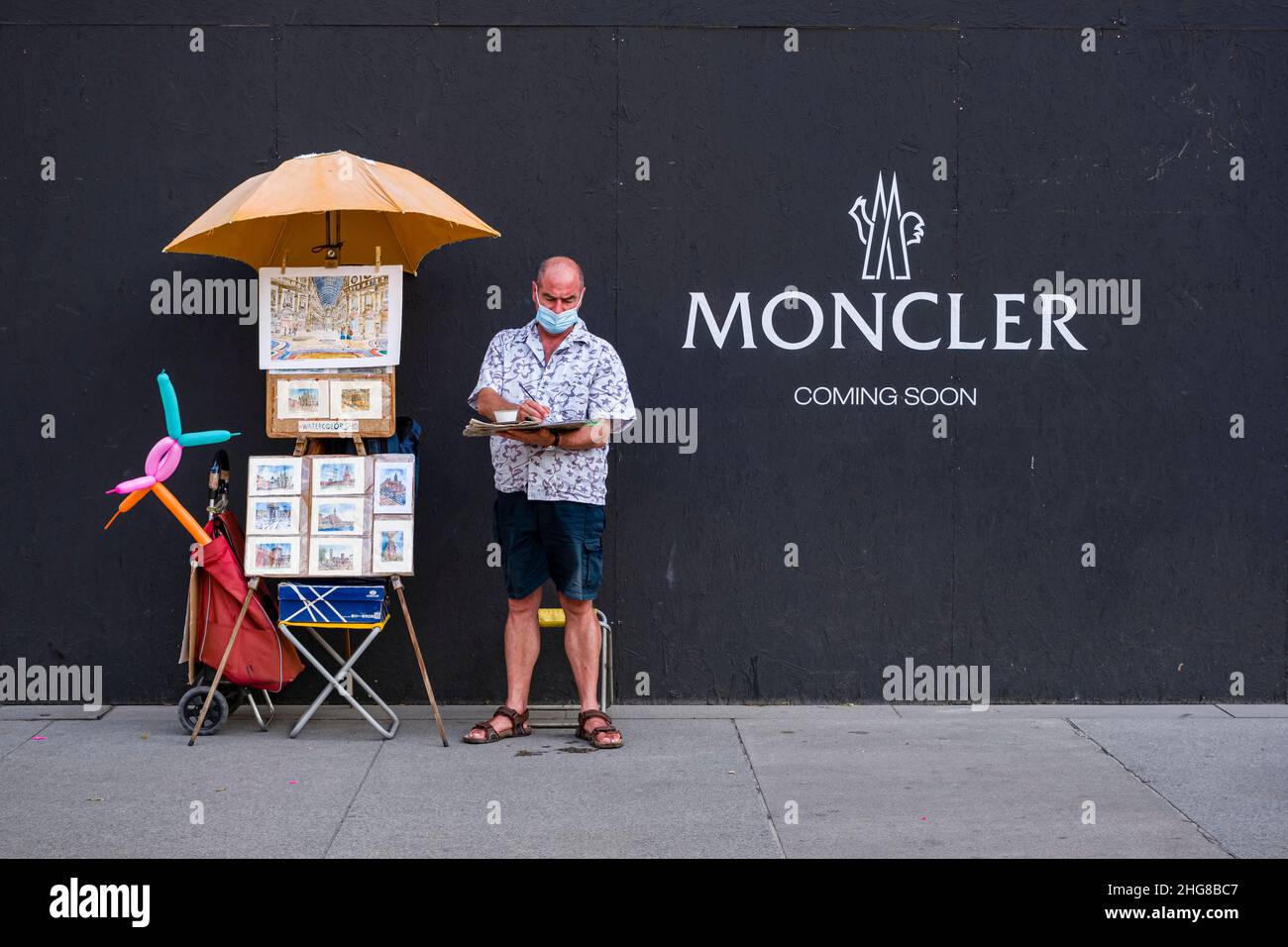 Ein Maler, der eine Gesichtsmaske trägt, arbeitet auf dem Bürgersteig vor einer Plakatwand. Stockfoto