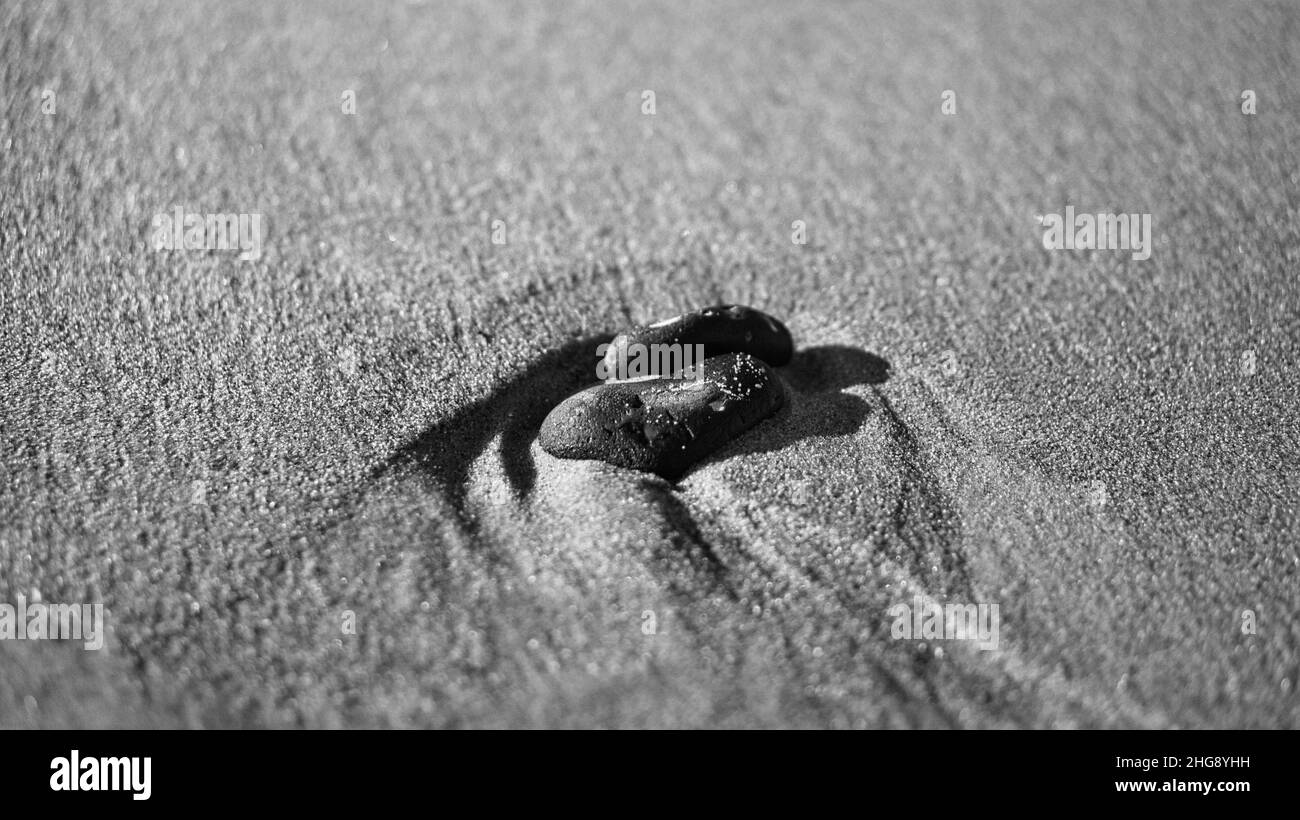 Herzförmiger Stein im Sand des Strandes an der Ostsee schwarz-weiß. Romantisches Symbol für verliebte Menschen. Kleines Zeichen als Stillleben. Stockfoto