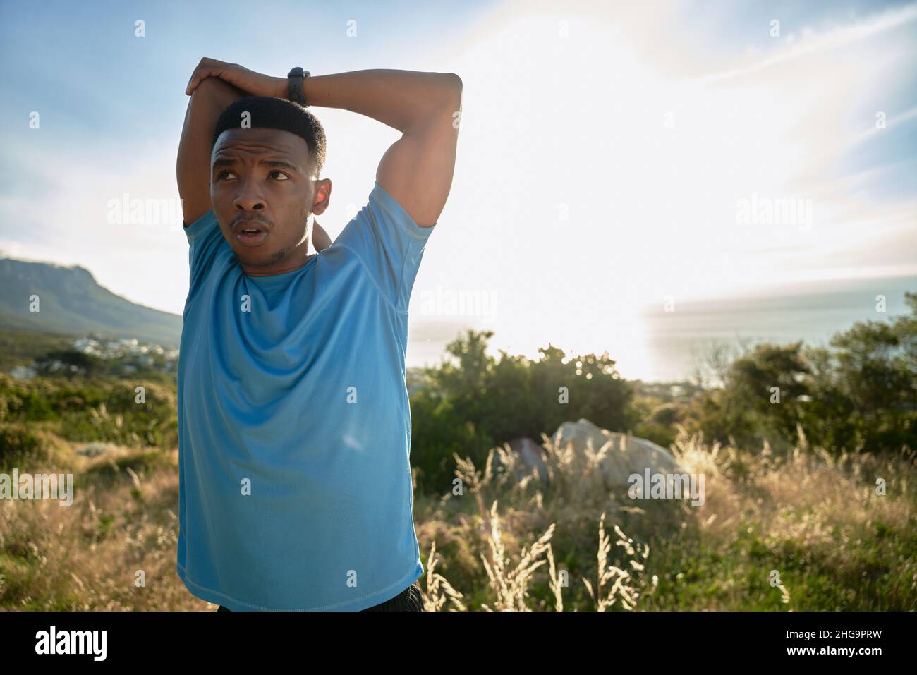 Schwarzer junger Erwachsener, der sich auf seinen täglichen Fitnessalltag am Berg vorbereitet. Wunderschöne Aussicht Stockfoto