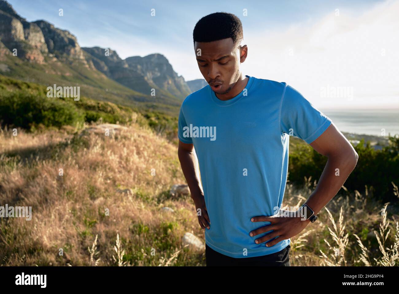 Schwarzer junger Erwachsener, der sich auf seinem Trail Run in den Berg den Atem raubt Stockfoto