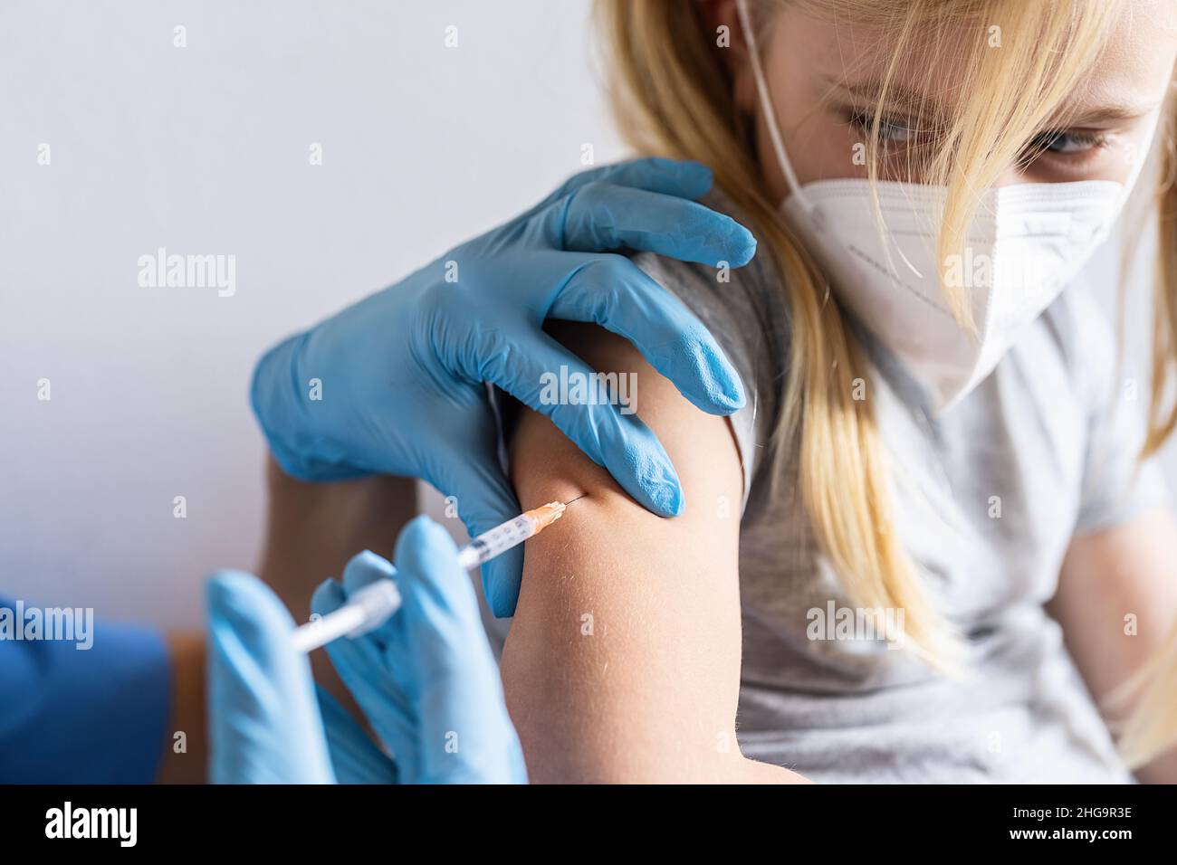 Erschreckenes blondes Mädchen, das die Spritze mit Impfstoff gegen Covid-19-Coronavirus, Grippe, gefährliche Infektionserreger von einem Arzt betrachtet. Während der Impfung Stockfoto