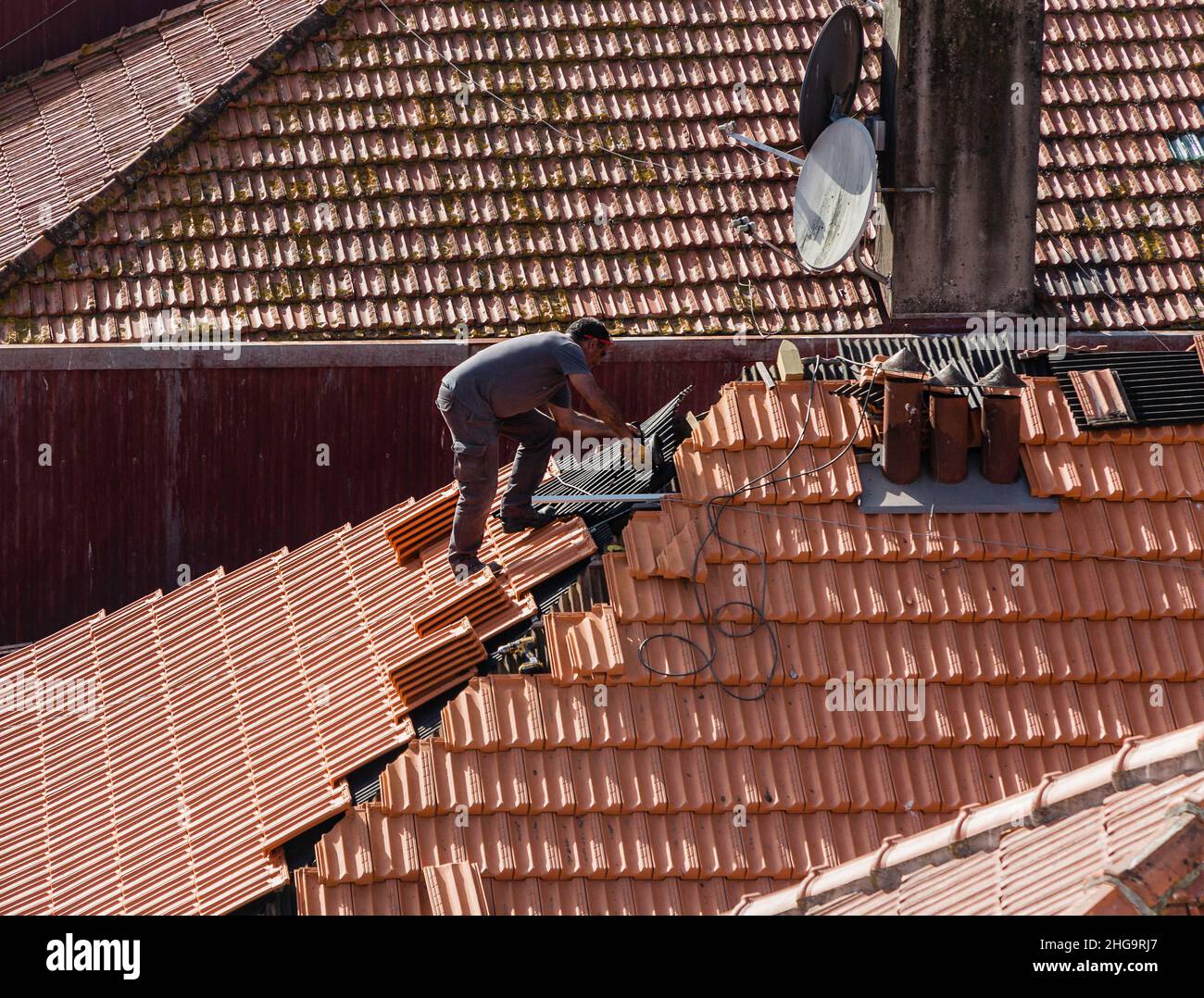 Ein Dachdecker ersetzt eines der vielen roten Ziegeldächer Portugals. Stockfoto