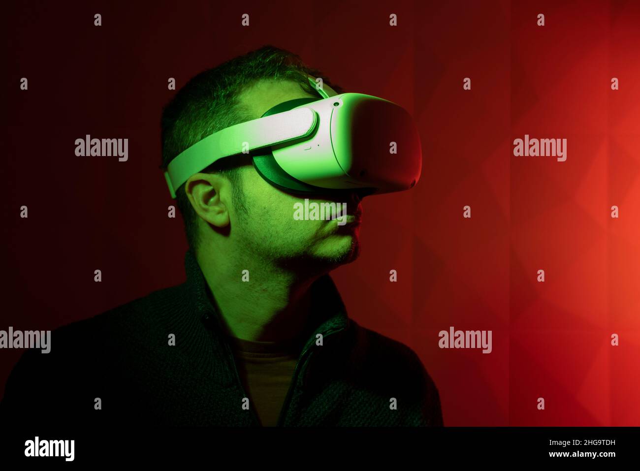 Mann mit weißer Virtual-Reality-Brille mit rotem Hintergrund und seitlichem grünem Licht Stockfoto