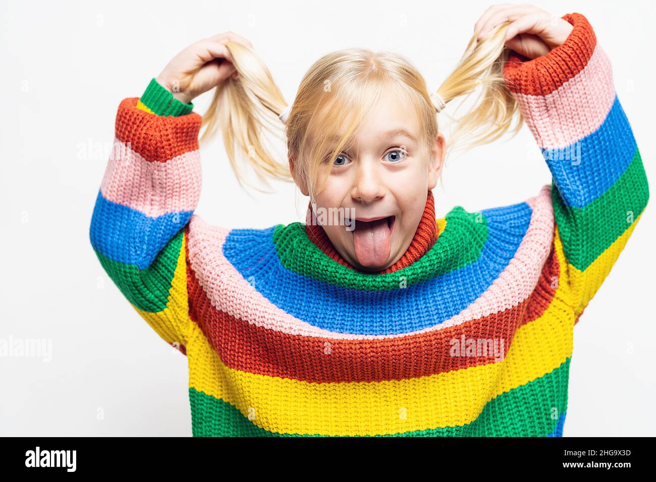 Kleine Mädchen ist erstaunt und ihre Hände berühren Brillen tragen Regenbogen-Stil Pullover und Zischerbrille isoliert auf weißem Hintergrund Stockfoto