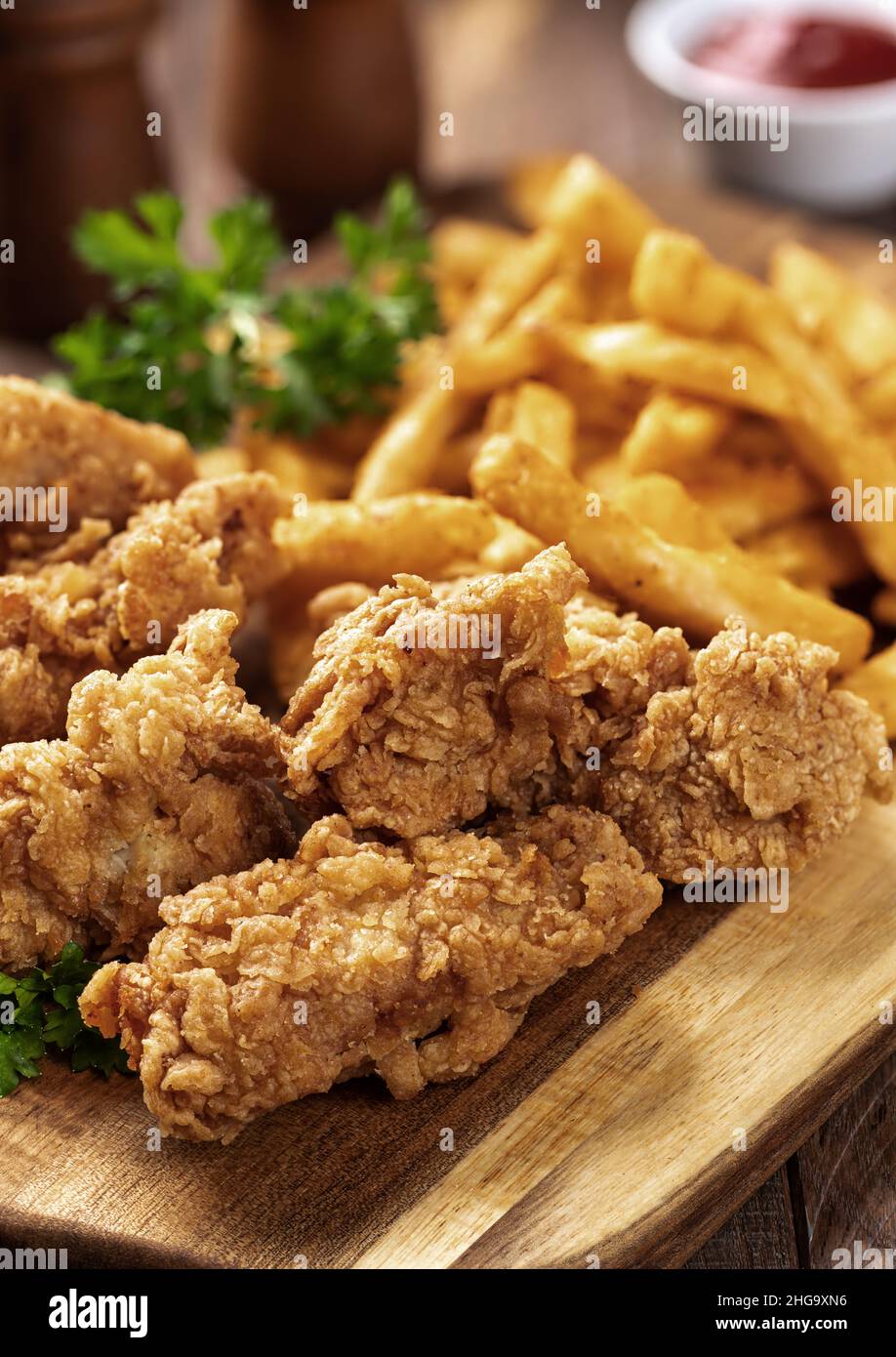 Knusprig gebratene Hähnchengerichte und pommes frites, garniert mit Petersilie auf einem hölzernen Schneidebrett Stockfoto