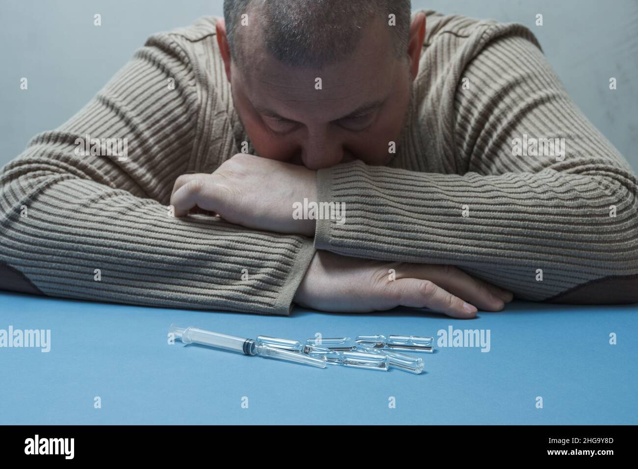 Der Mann am Tisch schaut nachdenklich auf die medizinische Spritze und Ampullen. Stockfoto