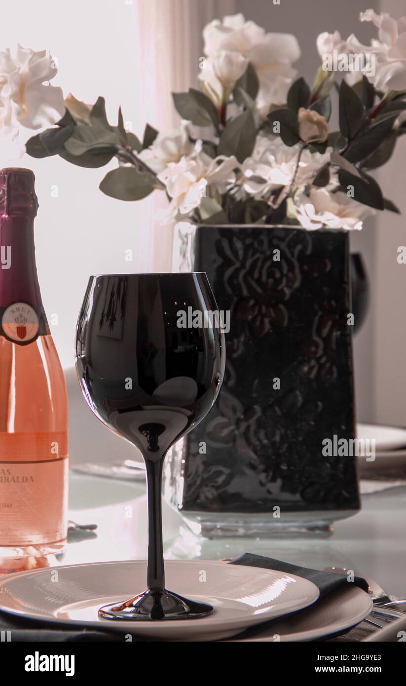 Schwarzes Weinglas mit einer Flasche rosa Champagner Cava und Blumenvase Stockfoto