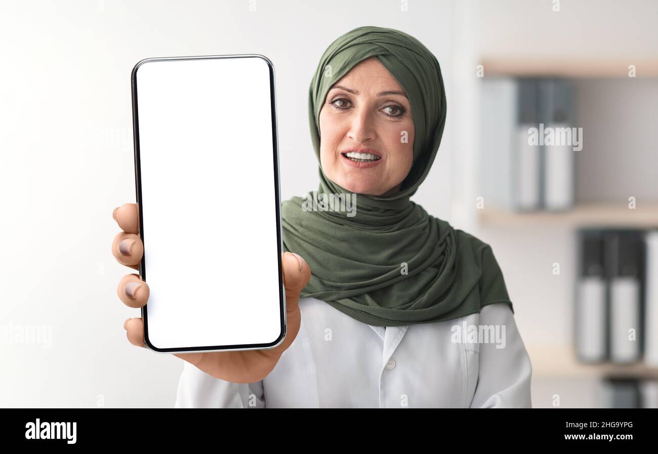 Ältere Muslimische Geschäftsfrau In Hijab Zeigt Blank Smartphone Mit Weißem Bildschirm Stockfoto Ältere Muslimische Geschäftsfrau In Hijab Zeigt Blank Smartphone Mit Weißem Bildschirm Stockfoto