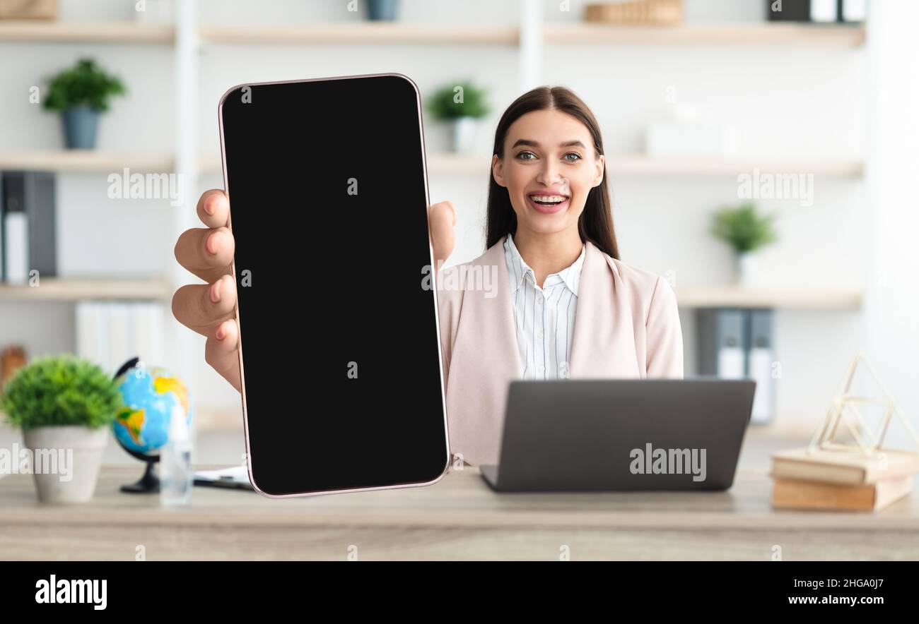 Mobiles Mockup. Lächelnde Dame Demonstriert Großes Unbeschriftete Smartphone, Während Sie Im Büro Sitzt Stockfoto