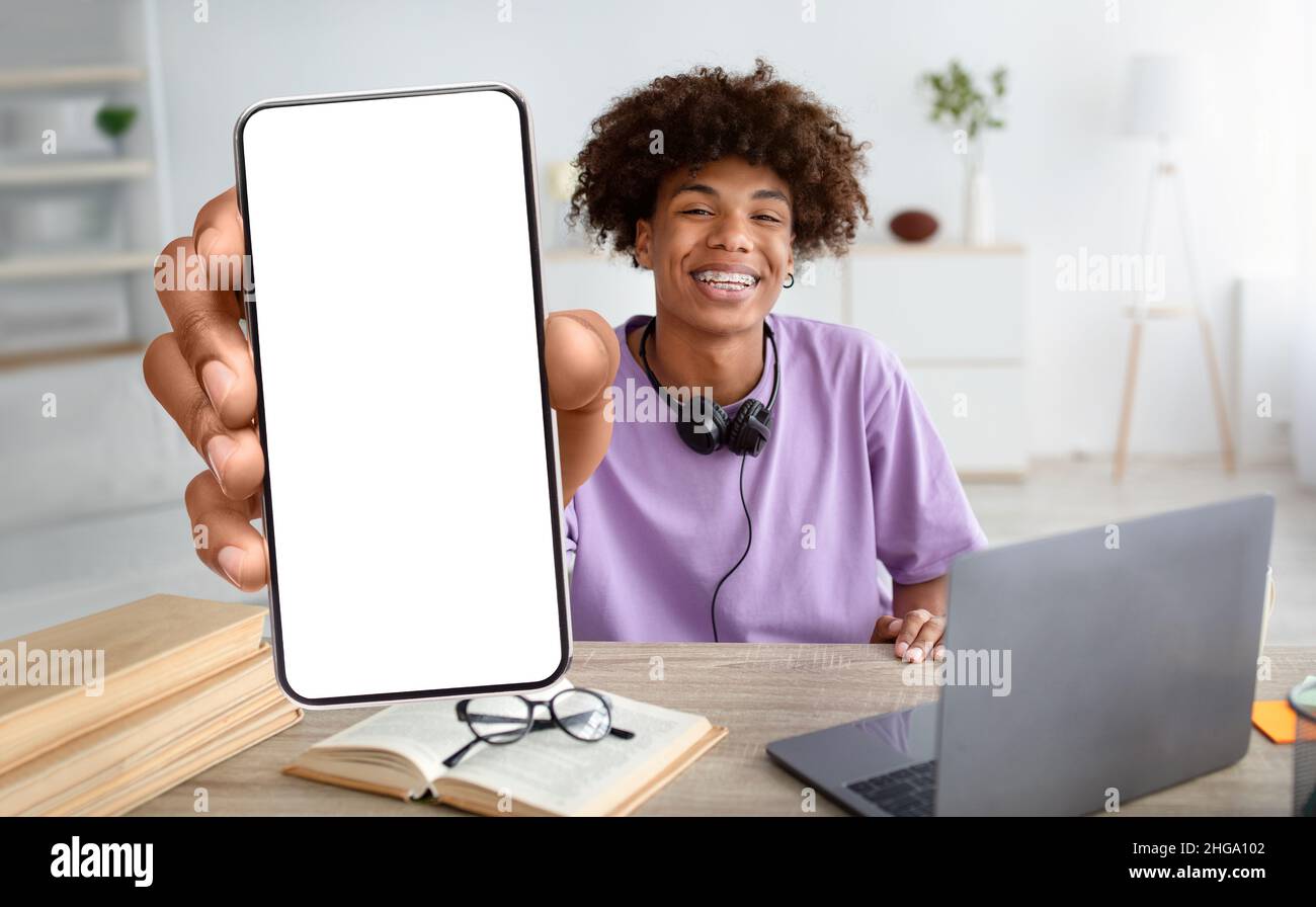 African American Teenage Guy Demonstriert Big Blank Smartphone Während Studie Zu Hause Stockfoto