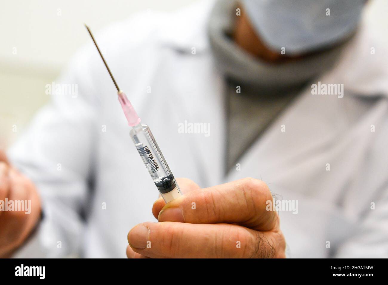 Die Abbildung zeigt einen Hausarzt, der in seinem Büro eine Impfung praktiziert, hält eine Spritze mit dem Impfstoff, bevor er einen Patienten impft Stockfoto