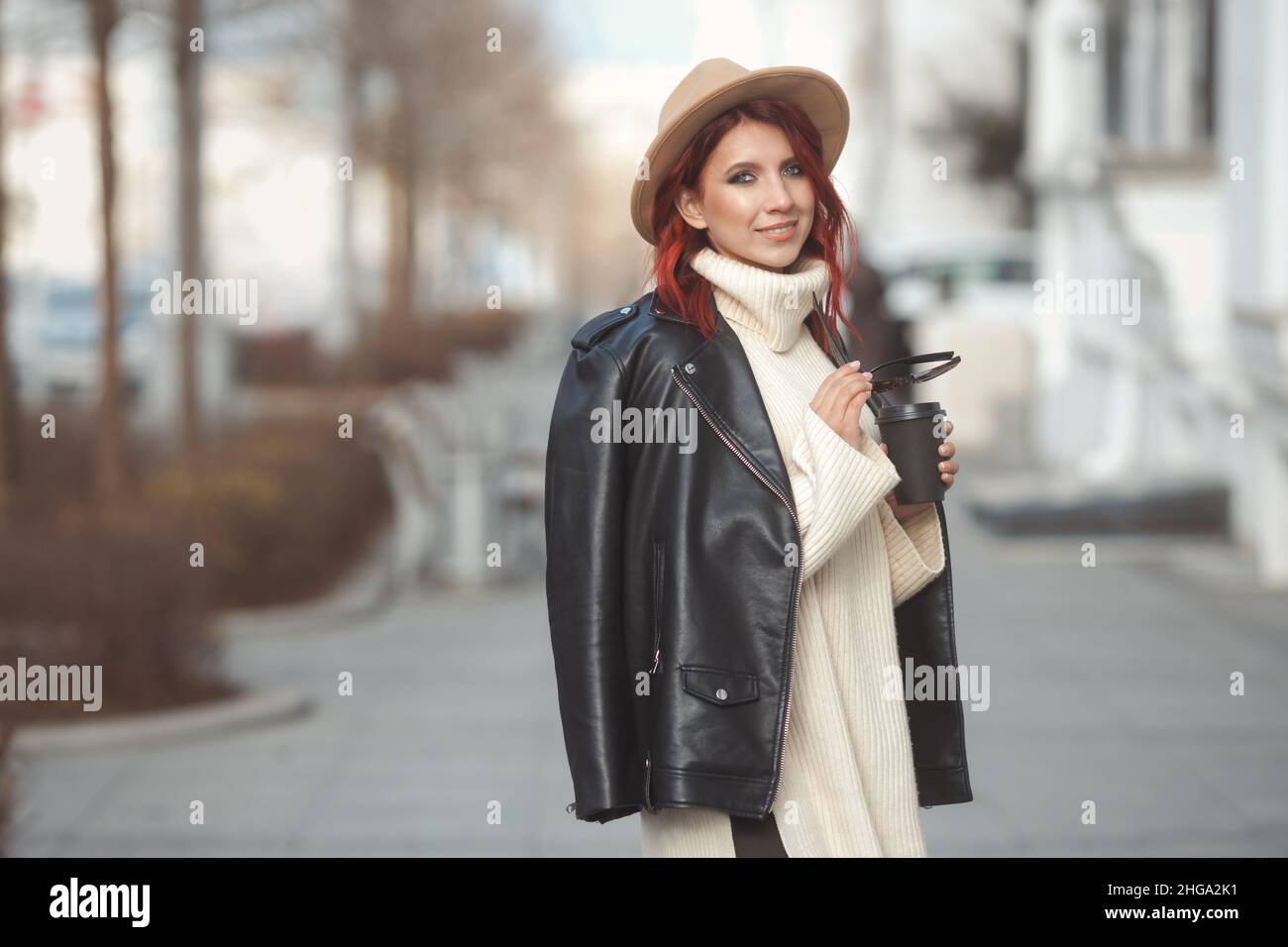 Stadtmodeportrait einer stilvollen tausendjährigen Frau in moderner Kleidung, die mit Kaffee auf der Straße der Stadt spazieren geht Stockfoto