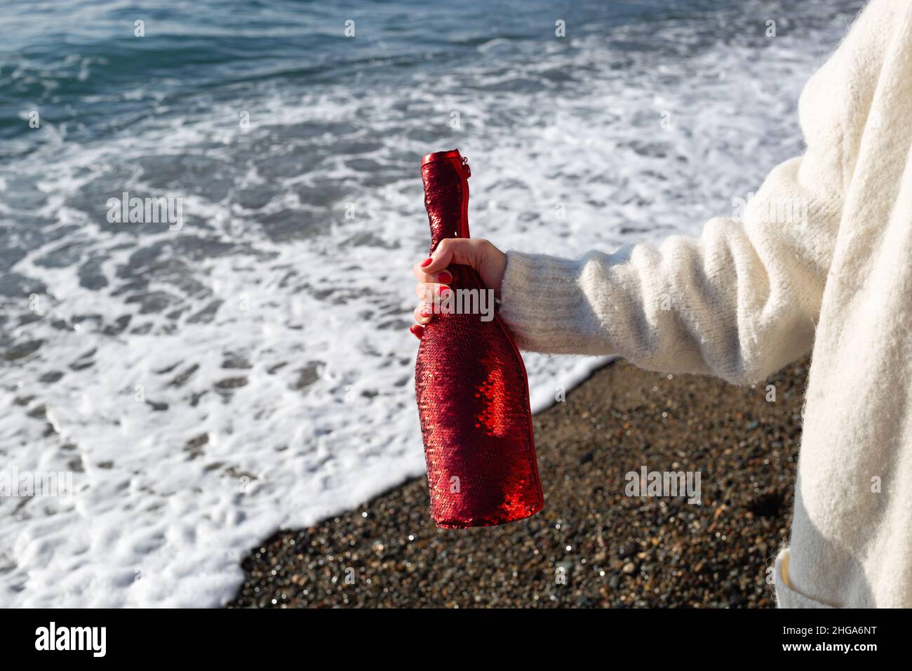 Frauenhand mit einer Flasche Champagner auf dem Hintergrund des Meeres. Stockfoto