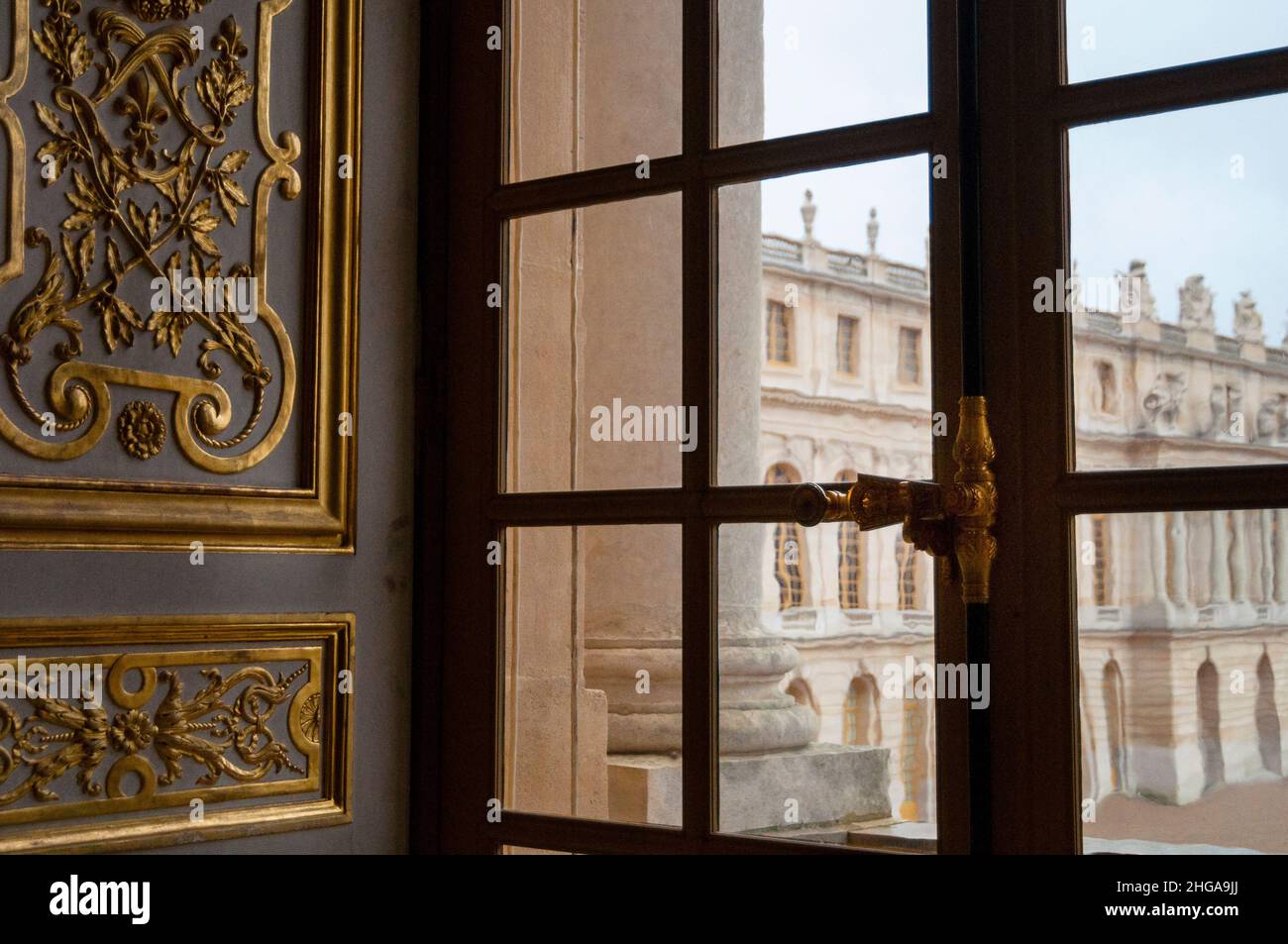 Ein verriegeltes Fenster im Schloss Versailles in Paris, eingerahmt von vergoldeten Basreliefverzierungen, Frankreich. Stockfoto
