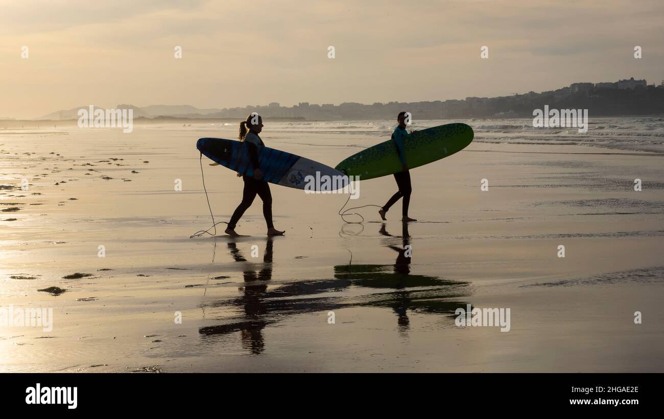 Zwei Sportler bereiten sich auf das Surfen im Wasser des Kantabrischen Meeres bei Sonnenuntergang vor. Stockfoto