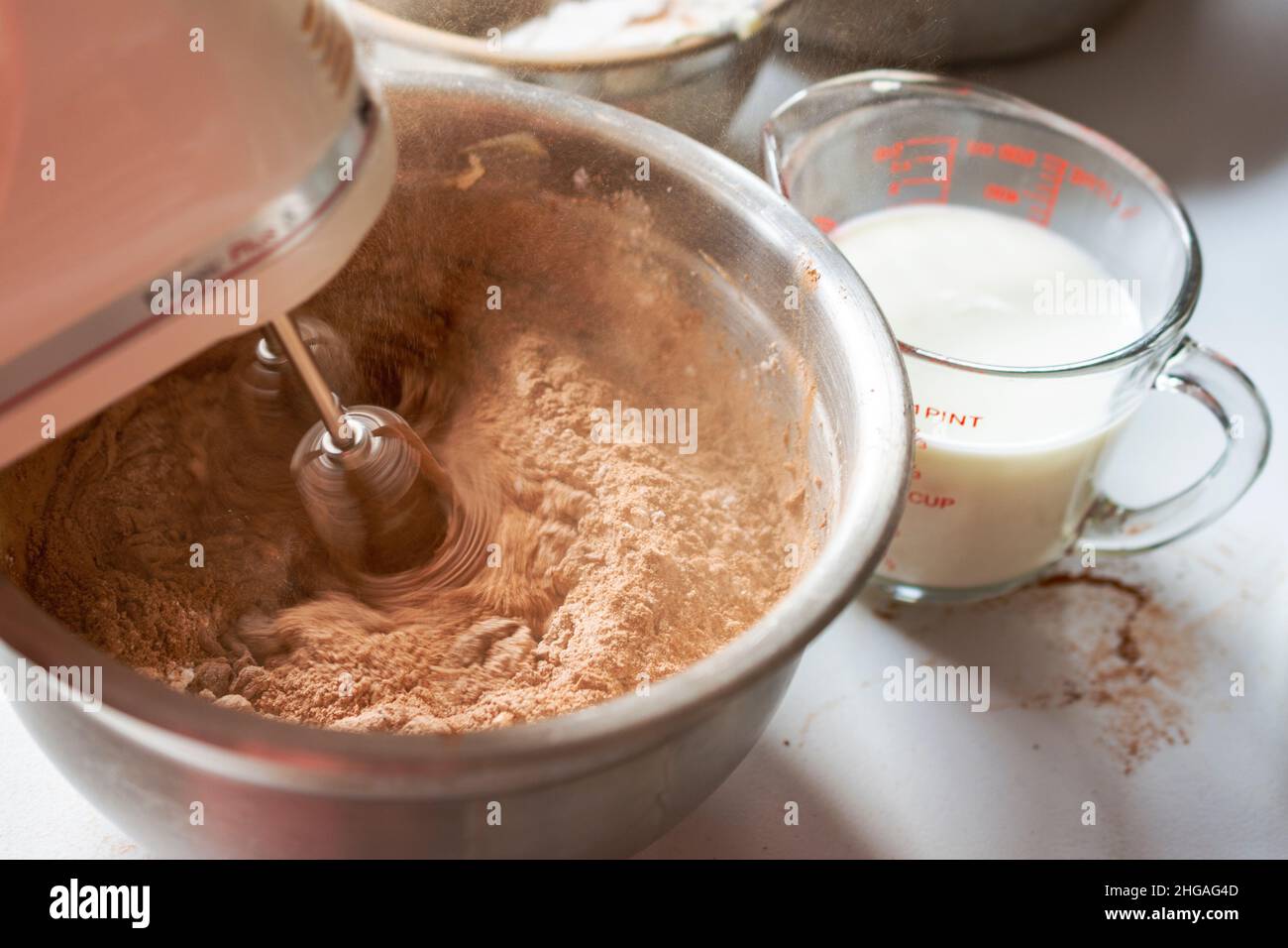 Herstellung eines Schokoladenkuchens: Hinzufügen von trockenen Zutaten. Rührbesen in Bewegung mit Bewegungsunschärfe. Stockfoto