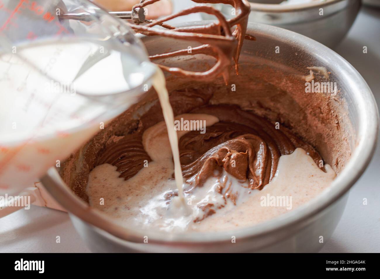 Herstellung eines Schokoladenkuchens: Hinzufügen von zusätzlicher Milch. Rührbesen sichtbar oben in der Mitte. Stockfoto