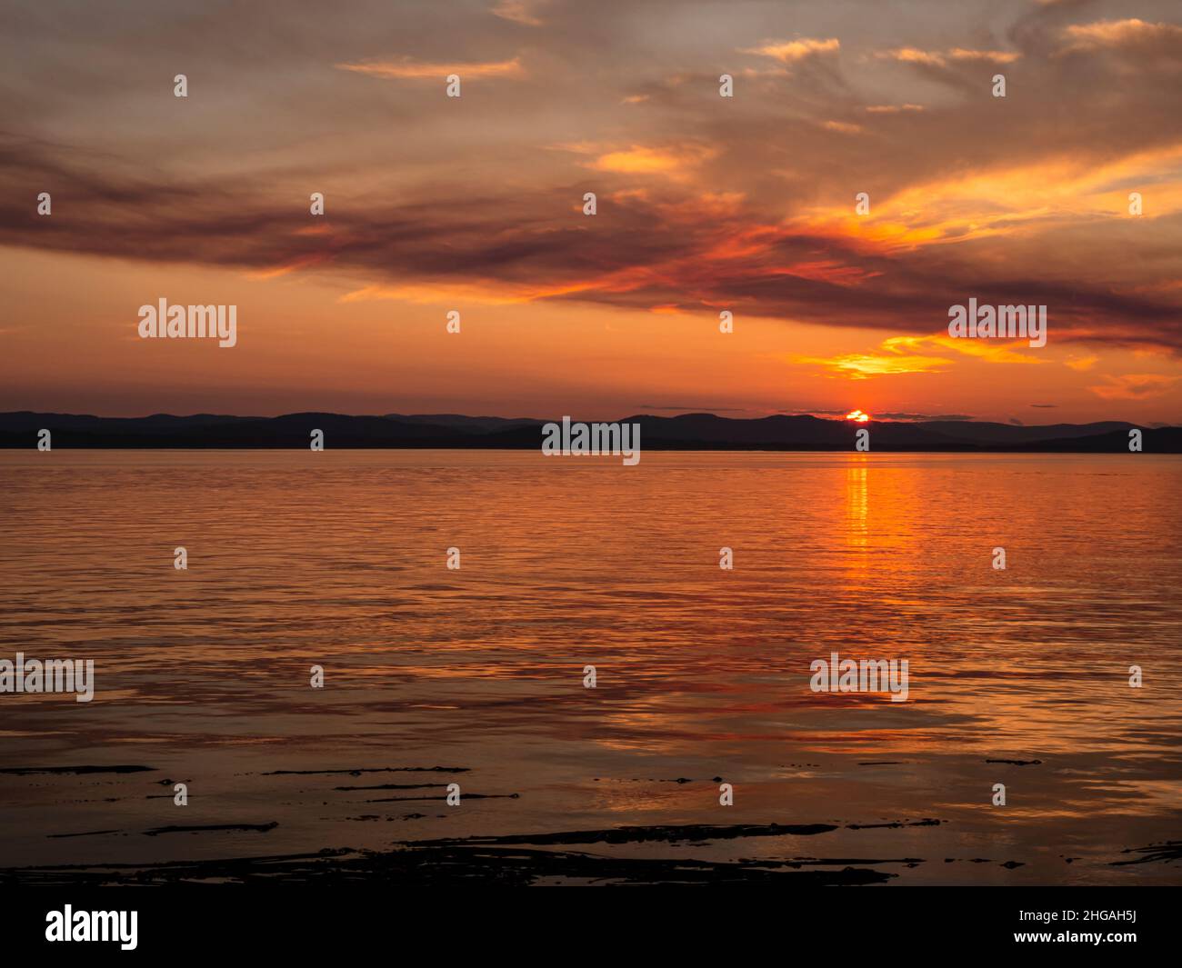 WA21155-00...WASHINGTON - Ein farbenfroher Sonnenuntergang, der durch den Rauch eines Waldfeuers auf Vancouver Island vom Lime Kiln State Park auf San Juan Island aus betrachtet wird. Stockfoto