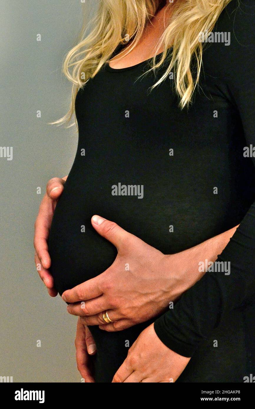 Mann hält den Babybauch einer in Schwarz gekleideten Schwangeren, Deutschland Stockfoto