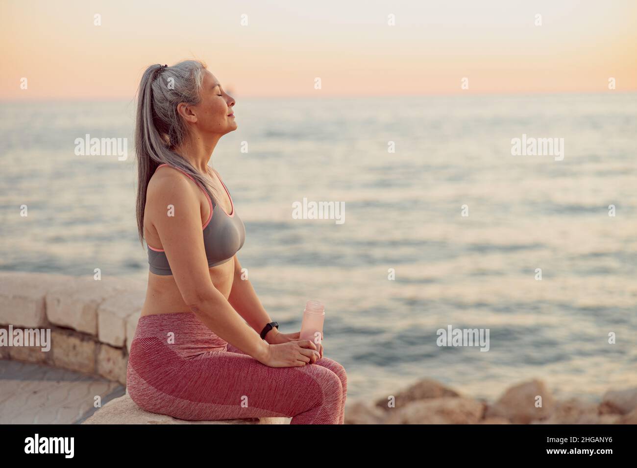 Reife Frau, die am Meer sitzt und den Sonnenuntergang genießt Stockfoto