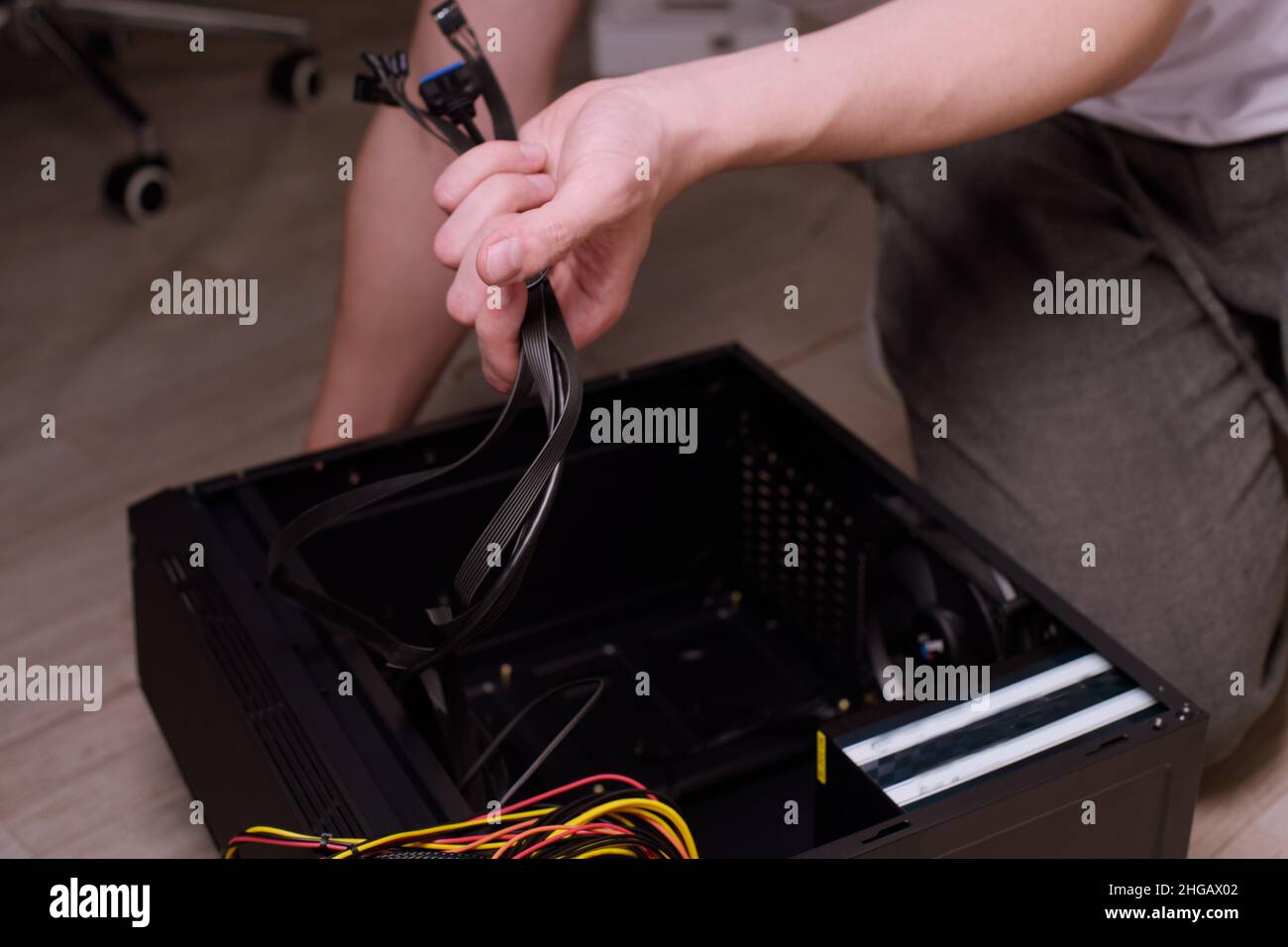 Ein Mann zu Hause sammelt, zerlegt einen Computer. Hände eines Mannes halten Drähte, verbindet Drähte. Sammeln eines Computers für Profis, ein Gaming-Computer Stockfoto