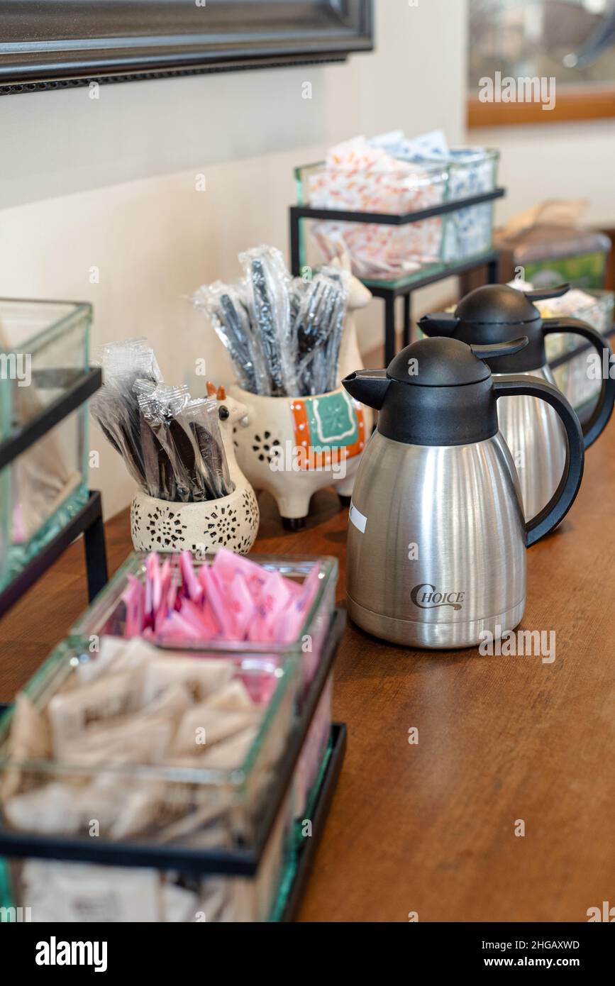 Creamer in einem isolierten silbernen Krug und Gewürze auf einer hölzernen Theke in einem Café. Stockfoto