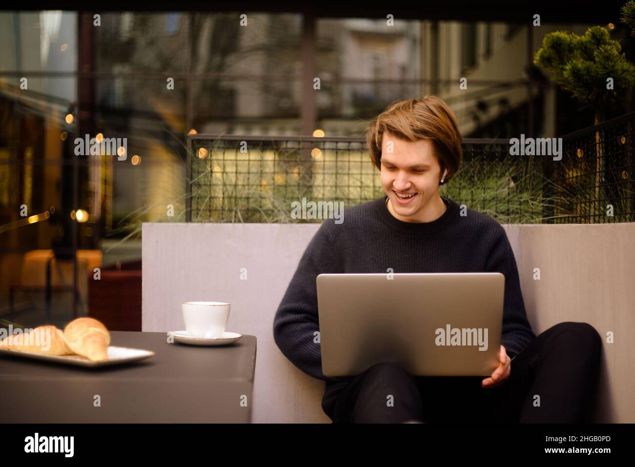 Mann trinkt eine Tasse Kaffee in einem Restaurant auf der Terrasse. Freiberufler im Freien mit einem Laptop, hat Frühstück mit Croissants. Businessman Looks and drea Stockfoto