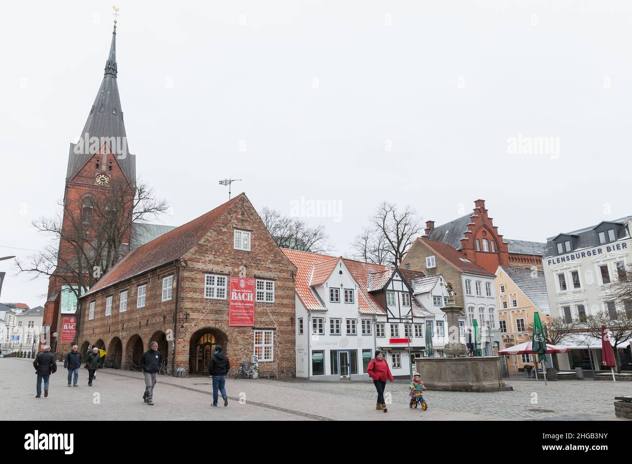 Flensburg, Deutschland - 9. Februar 2017: Nordermarkt, Stadtplatz mit Neptunbrunnen und Marienkirche. Gewöhnliche Menschen gehen die Straße entlang Stockfoto