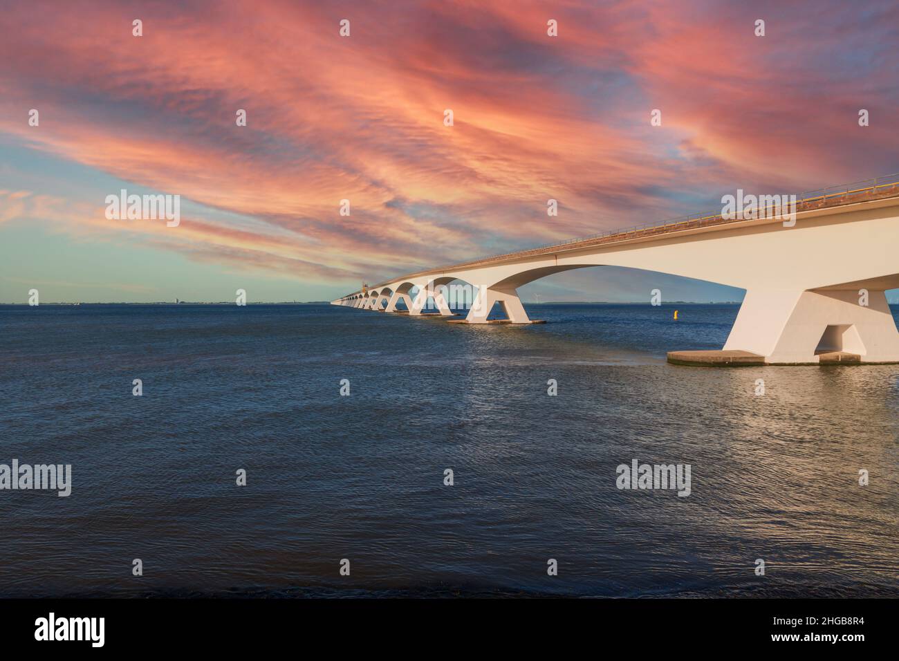 Zeeland Bridge - lange weiße Brücke über den Fluss, schöner blauer Himmel mit dynamischen Wolken. Lange Zeit, ruhiges Wasser der Oosterschelde. Sonnenuntergang. Stockfoto