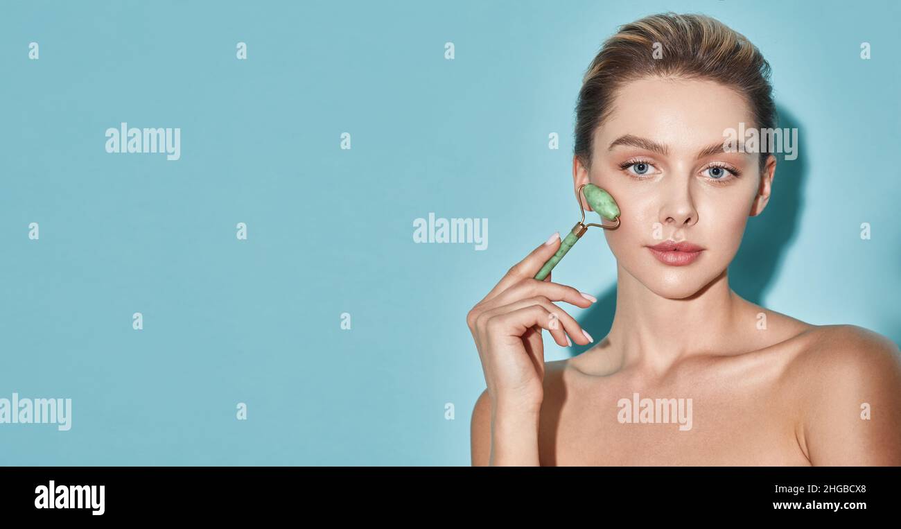 Jadewalze im Gesicht. Frau massiert ihr Gesicht mit einer grünen Jadewalze für eine elastische, perfekte Haut Stockfoto