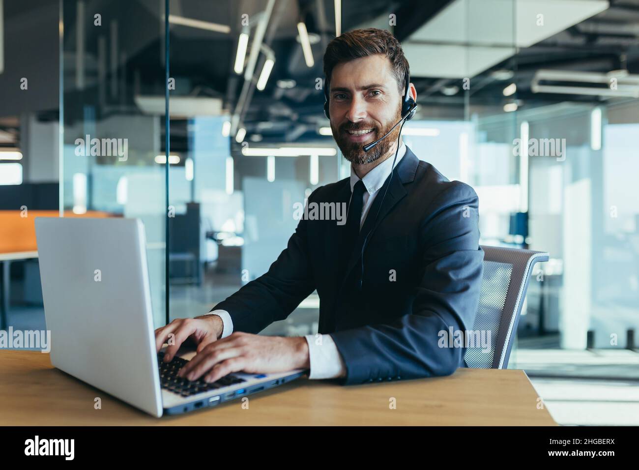 Ein Mitarbeiter des Callcenters schaut auf die Kamera und lächelt nutzt ein Headset für ein Video dink, ein Geschäftsmann macht ein Online-Meeting mit einem Laptop Stockfoto