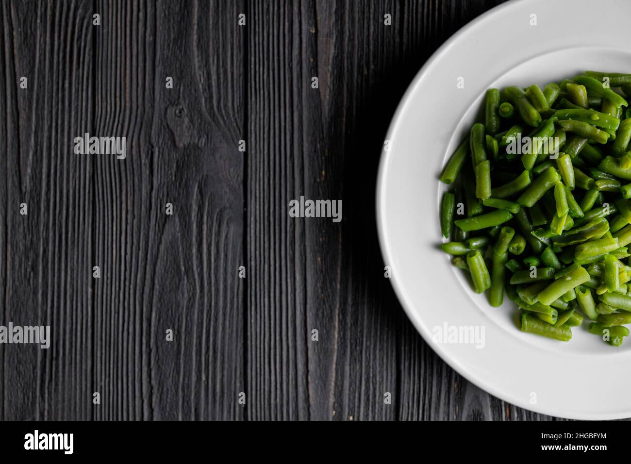 Servieren von grünen Bohnen weißen Teller auf dunklem Holzbrett, Low-Key-Foto mit Kopierplatz. Stockfoto