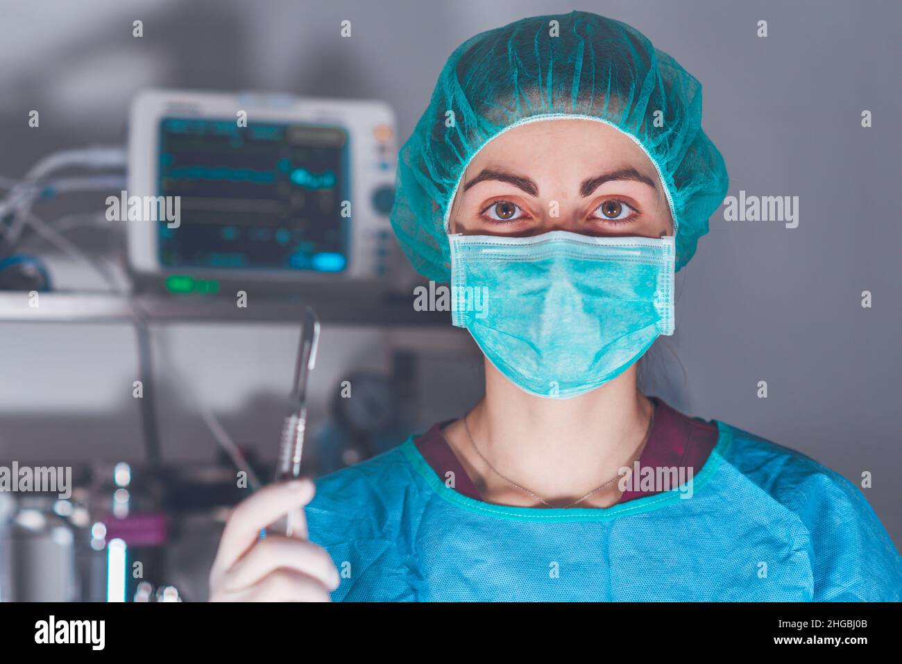 Erwachsene Frau in medizinischer Maske und Hut und mit Skalpell Blick auf die Kamera vor der Operation im Krankenhaus. Hochwertige Fotos Stockfoto