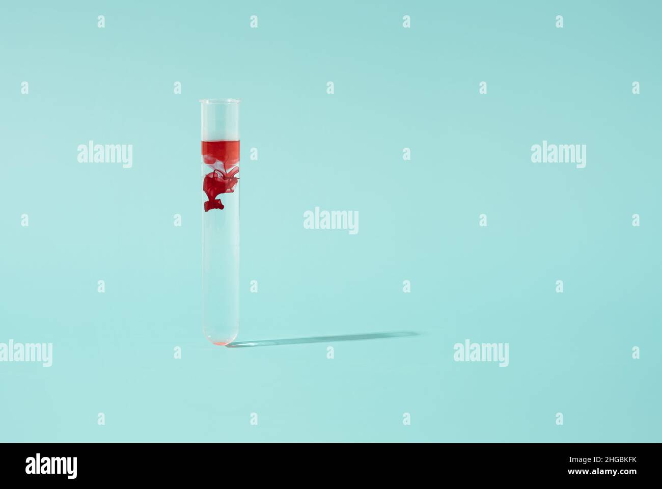 Reagenzglas mit einem Tropfen Blut auf pastellblauem Hintergrund. Minimales Konzept der medizinischen Analyse. Stockfoto