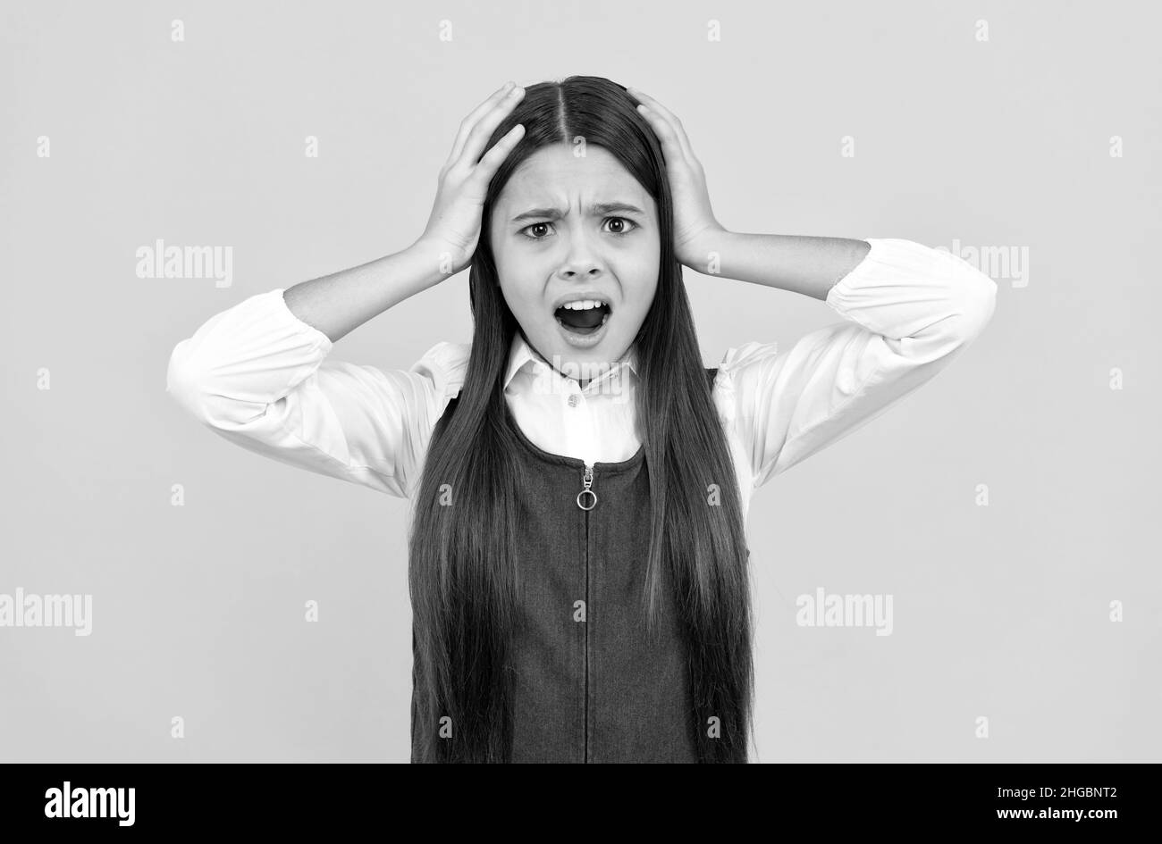 Schockiert Teenager-Mädchen in Schuluniform nehmen Kopf in die Hände gelben Hintergrund, Schock Stockfoto