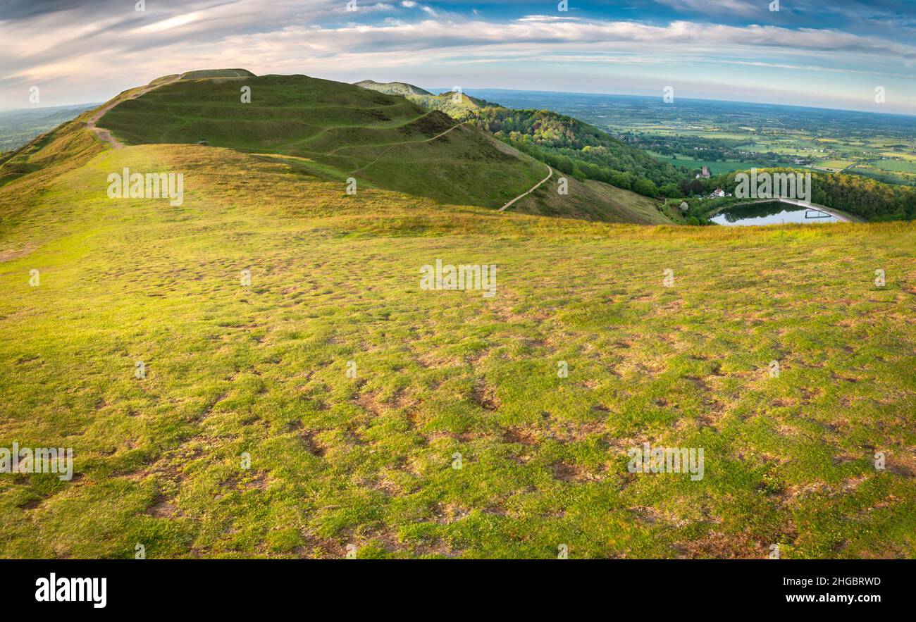 Niedrig angewinkelte Sommermorgensonne, die den Gipfel und die Wege der Malvern Hills beschneiden, strukturierte üppige, grüne, grasbedeckte Hänge und detaillierte Grate. Stockfoto