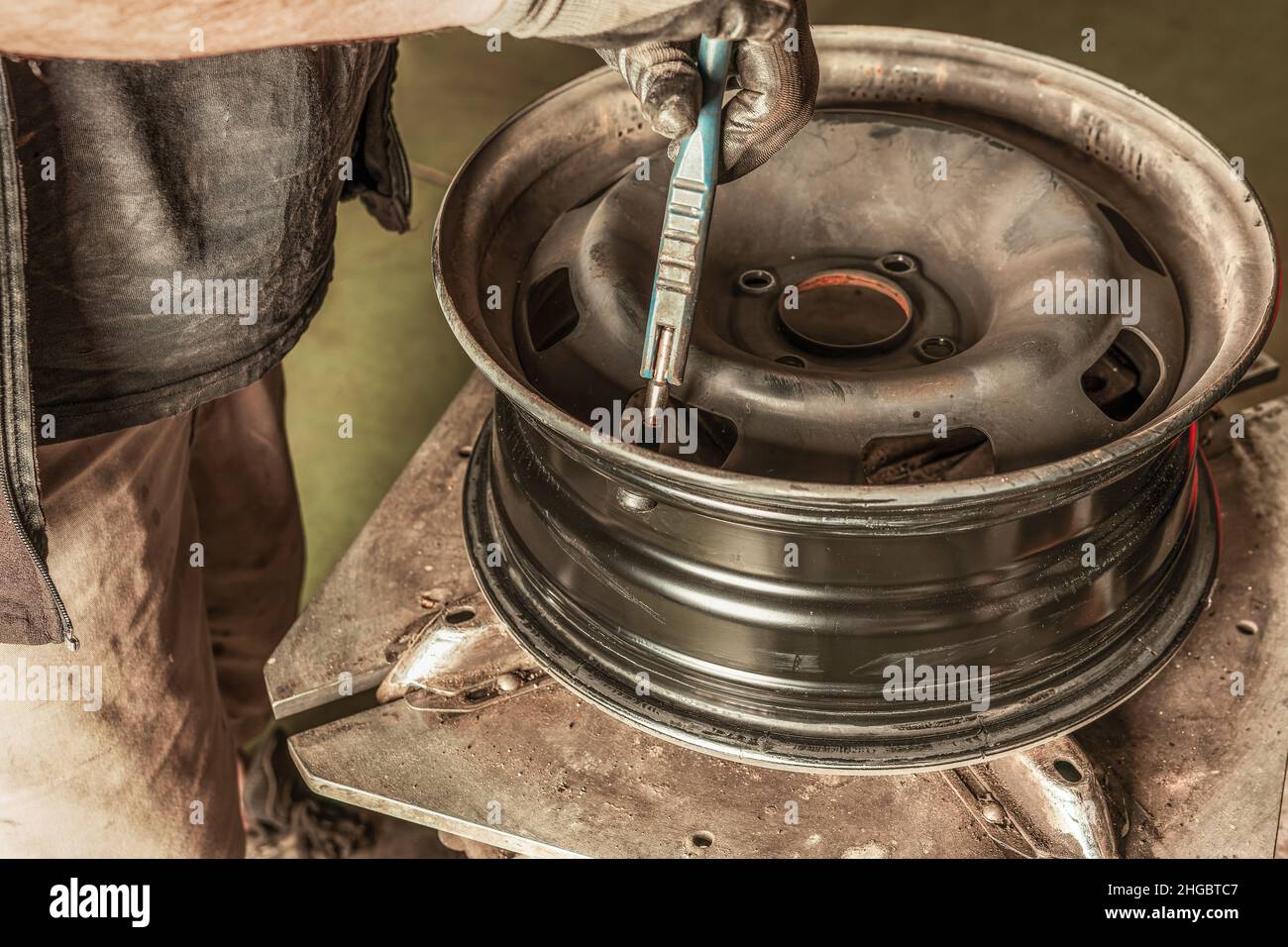Mann, der ein Ventil in ein Rad setzt, das er in einer schmutzigen Garage repariert Stockfoto